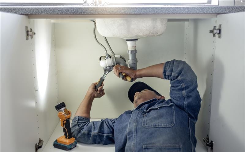 Plumber repairing pipes beneath a bathroom sink in San Clemente